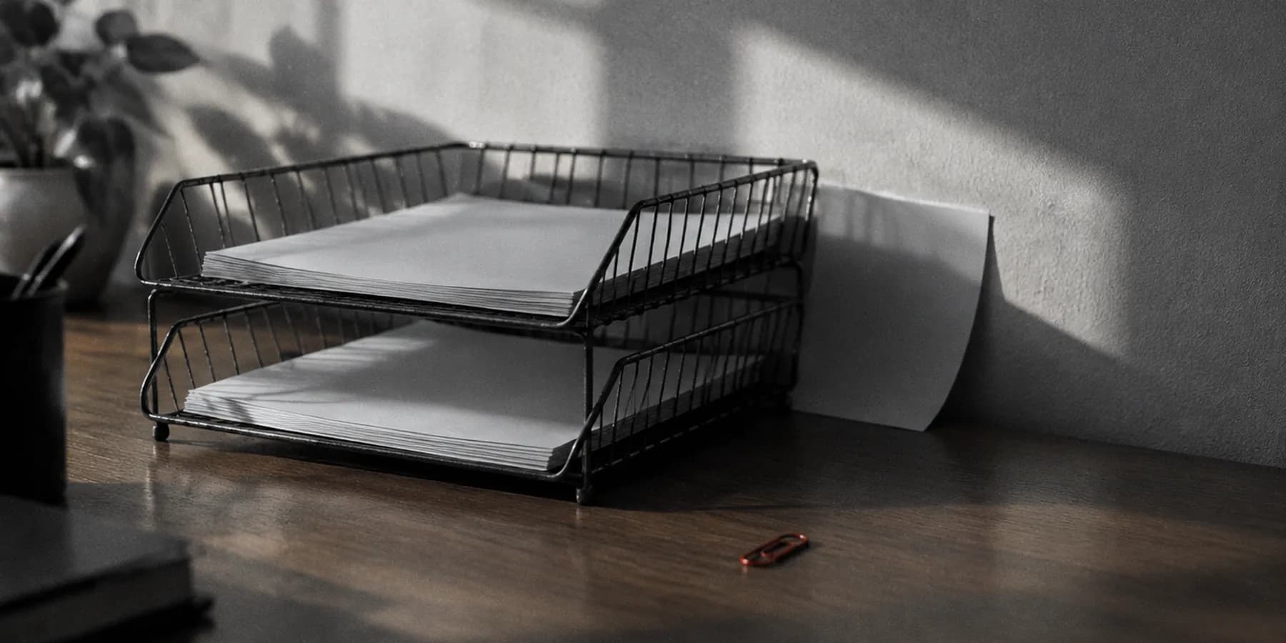 Una bandeja de oficina de dos pisos con una hoja caída por detrás, contra la pared