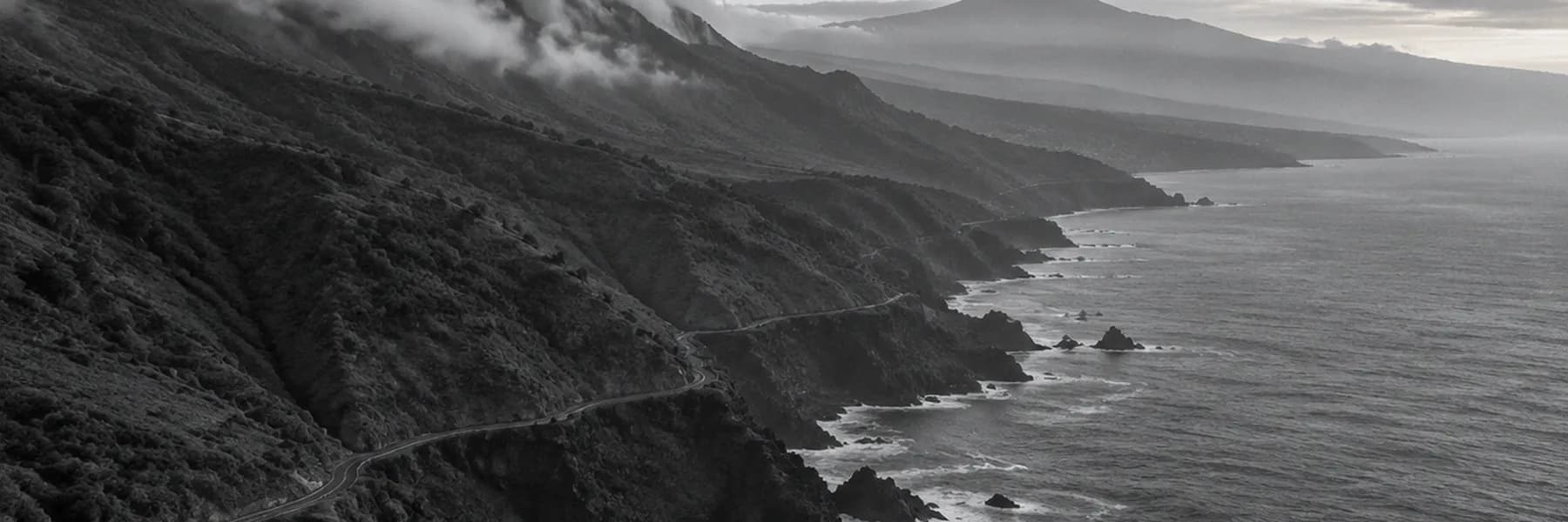 The north coast of Tenerife at dawn, clouds spilling over the ridge and Mount Teide in the distance